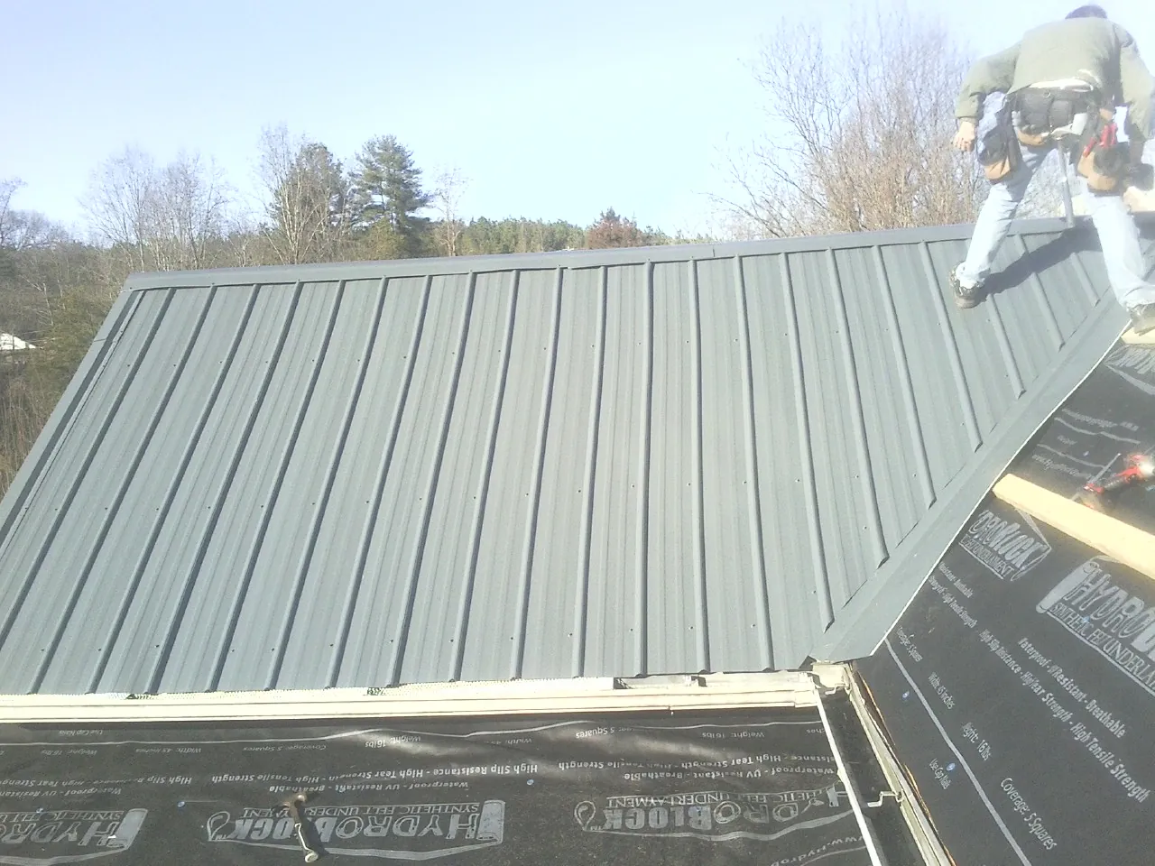 Crew installing dark green standing seam panels over synthetic underlayment in Jersey Shore