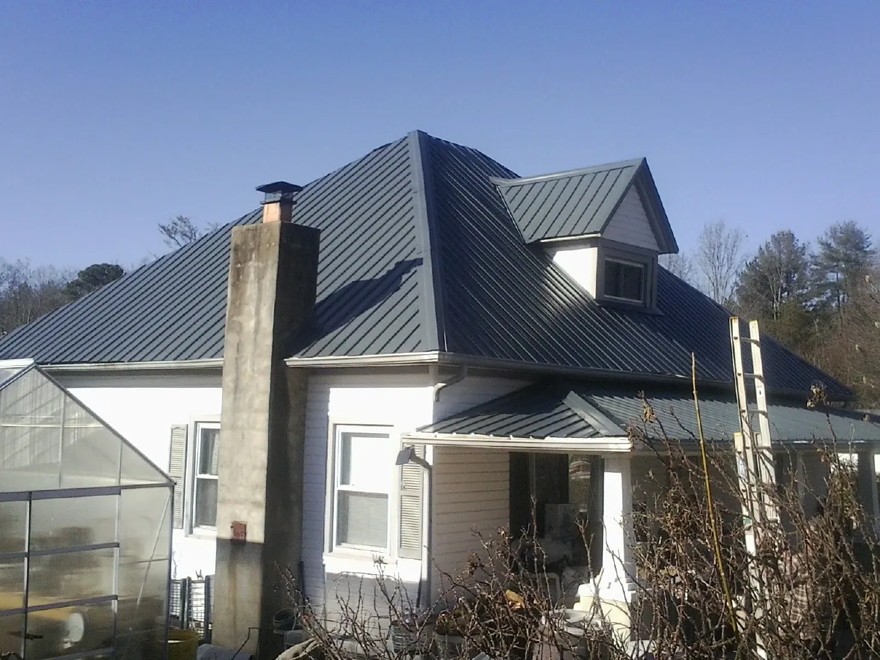 Dark blue standing seam metal roof on a white farmhouse with dormer — Slate & Tile Roof Repair by Roofing Brothers in Jersey Shore