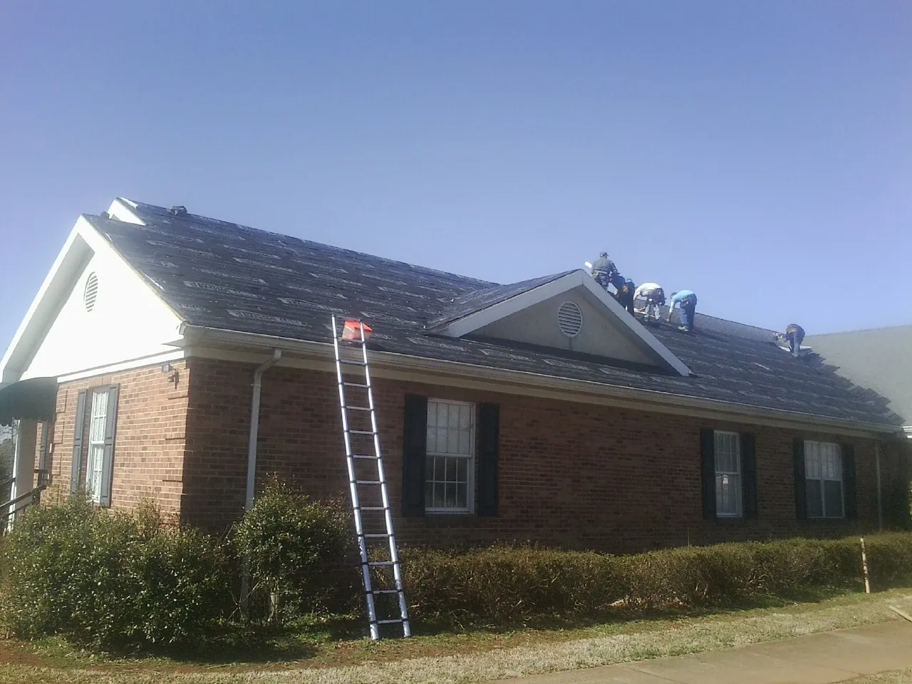 Crew tearing shingles off a brick ranch roof with a ladder set — Metal Roof Repair work by our crew in Jersey Shore