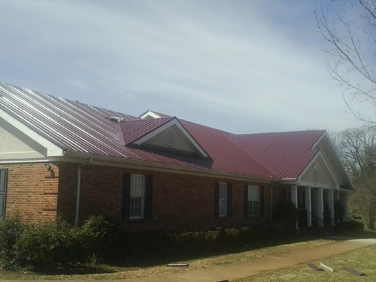 Red metal roof with gabled entries on a long brick building, from a Hail Damage Roof Repair job in Jersey Shore