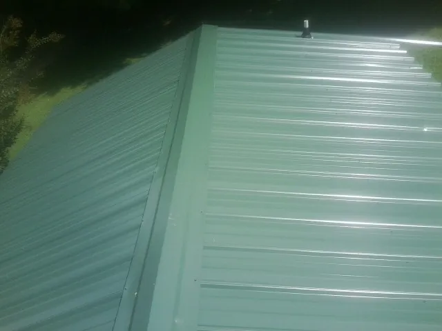 New green metal panels meeting at the ridge of a roof — Flat Roof Repair work by our crew in Jersey Shore