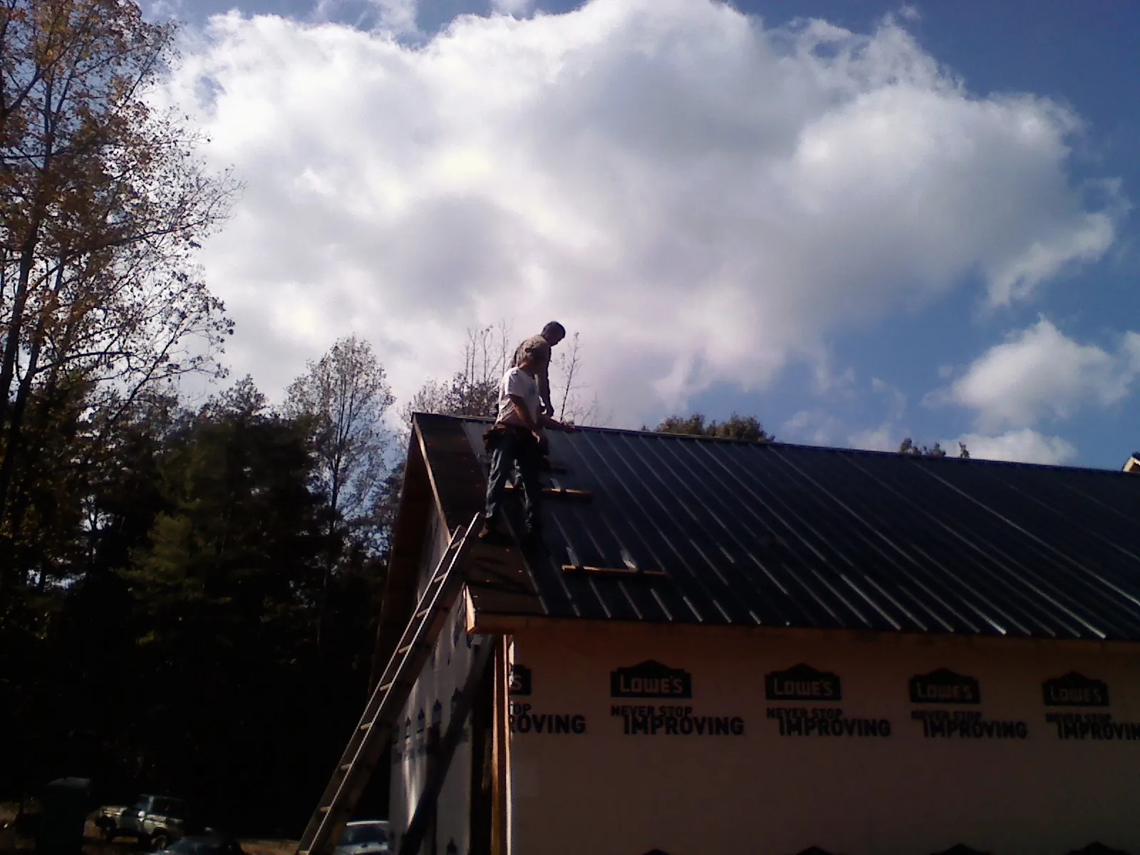 Roofer fastening dark metal panels high against a cloudy sky, from a Roof Inspection job in Jersey Shore