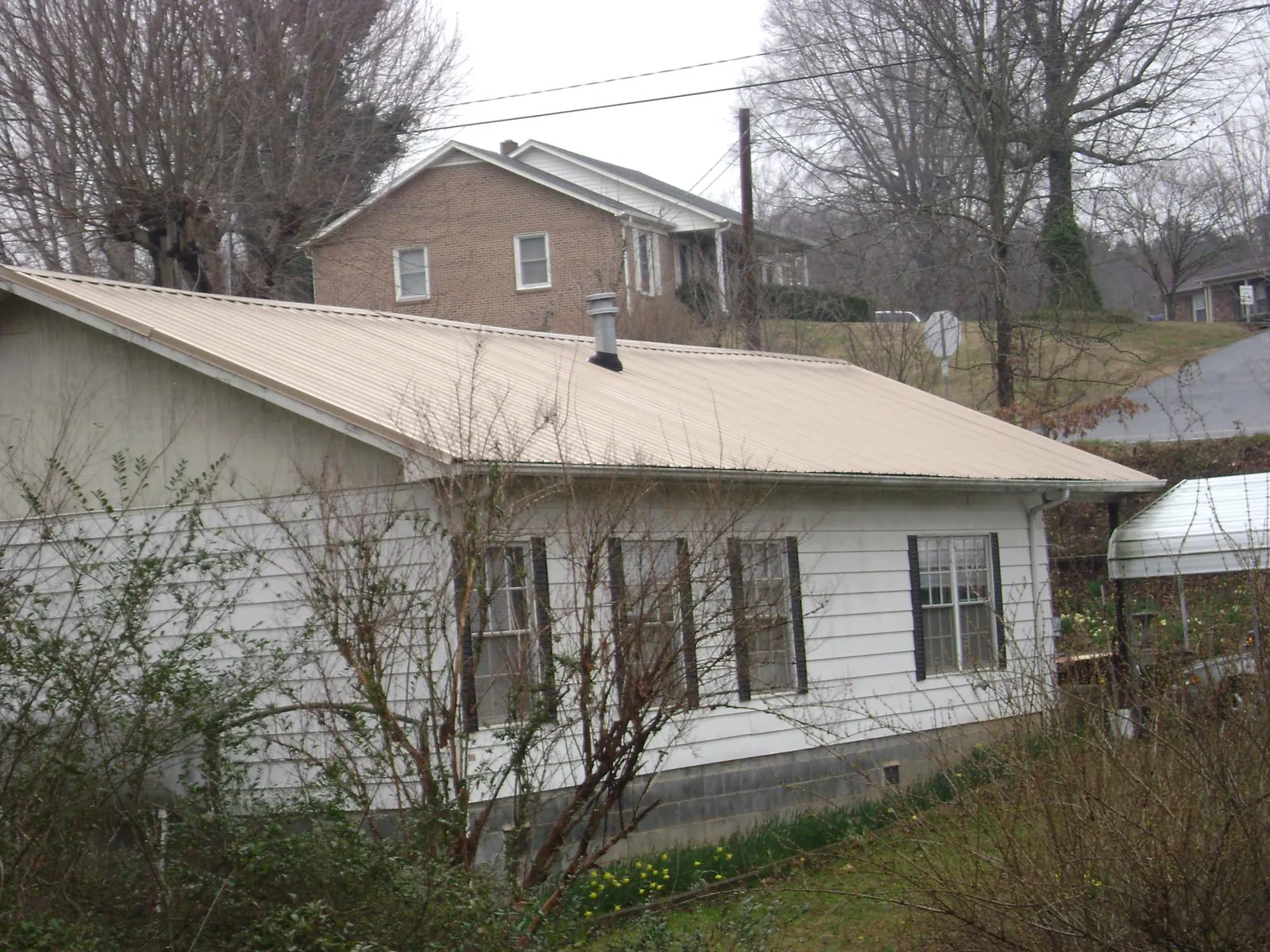 Tan metal roof on a white sided house set into a hillside — Commercial Roofing by Roofing Brothers in Jersey Shore